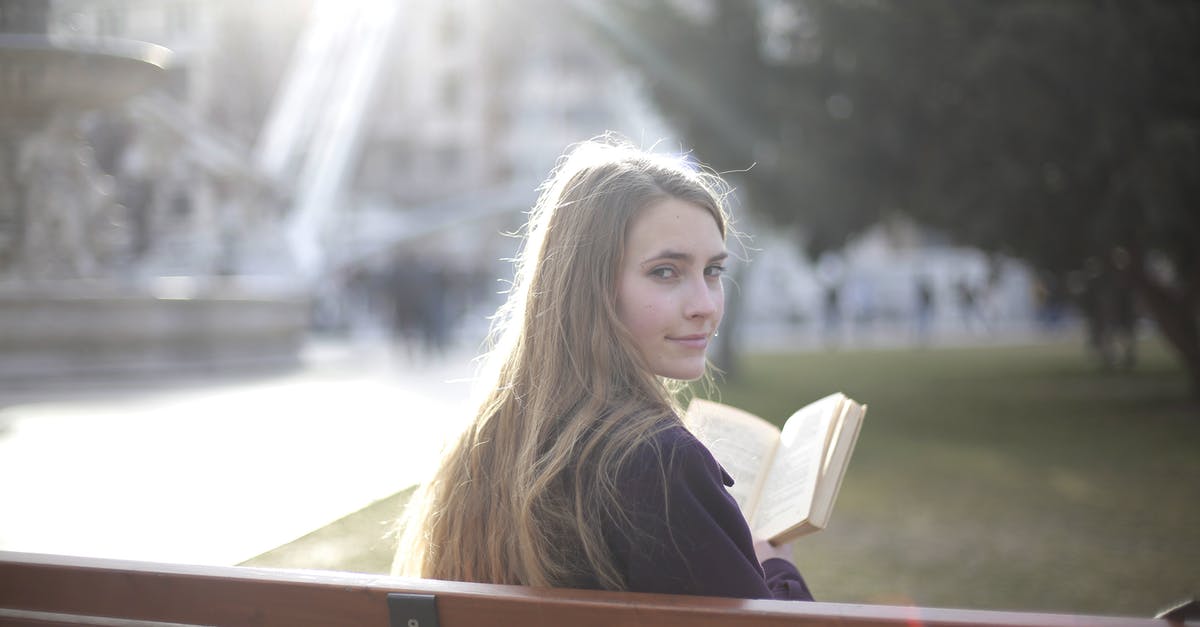 Is my story over? - Back view of peaceful female in casual jacket sitting on wooden bench in city park and enjoying story while relaxing and looking over shoulder