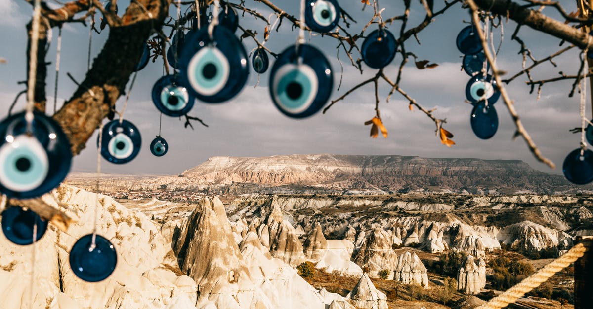 Is switching region considered smurfing? - Nazar amulets on threads hanging from tree branches near rocky uneven formations with mountains and grass with plants in Turkey in Cappadocia region under gray cloudy sky in summer day