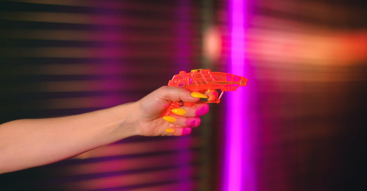 Is there a better way to aim and shoot? - Crop anonymous female with manicured hand pointing toy gun against neon lights in dark studio