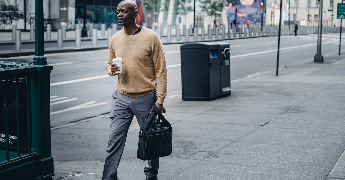 Is there a way to keep the BGM going while paused? - Full body of pensive African American male walking on pavement near asphalt road with takeaway coffee and black handbag in hand