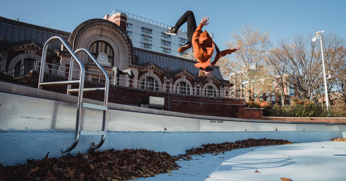 Is there any danger in chopping down every tree I see? - Side view of agile male athlete performing break dance backflip while jumping in air under blue sky in autumn town