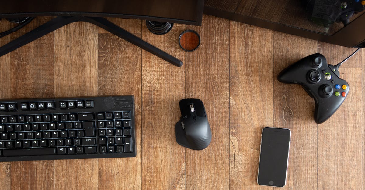 Lag on old PC games until a gamepad is connected - Top view of black gamepad with mouse and keyboard on wooden desk with monitor in apartment in daytime