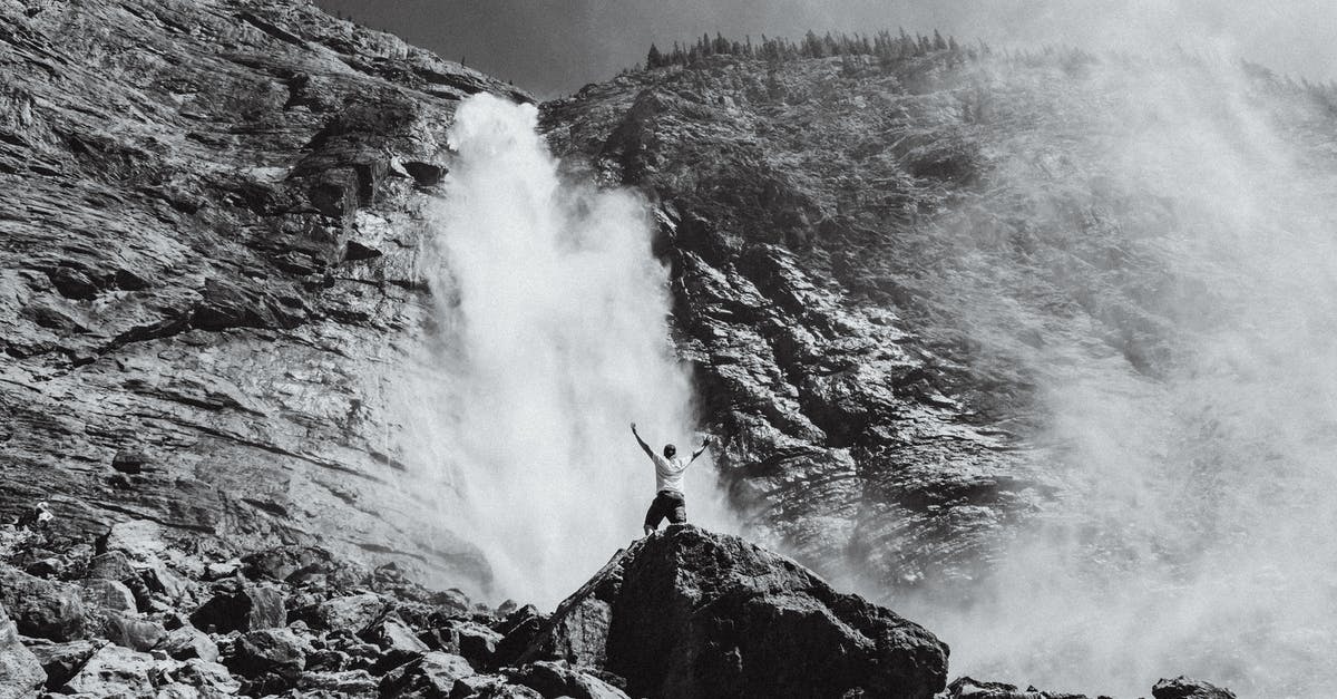 Long-distance fluid handling with pipes - Black and white of anonymous male enjoying fast stream of foamy waterfall on rough formation