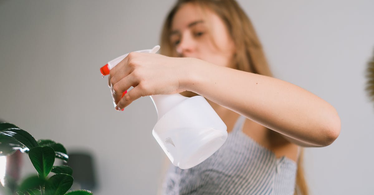 Long-distance fluid handling with pipes - Long haired lady using white spray bottle for green plant in selected focus