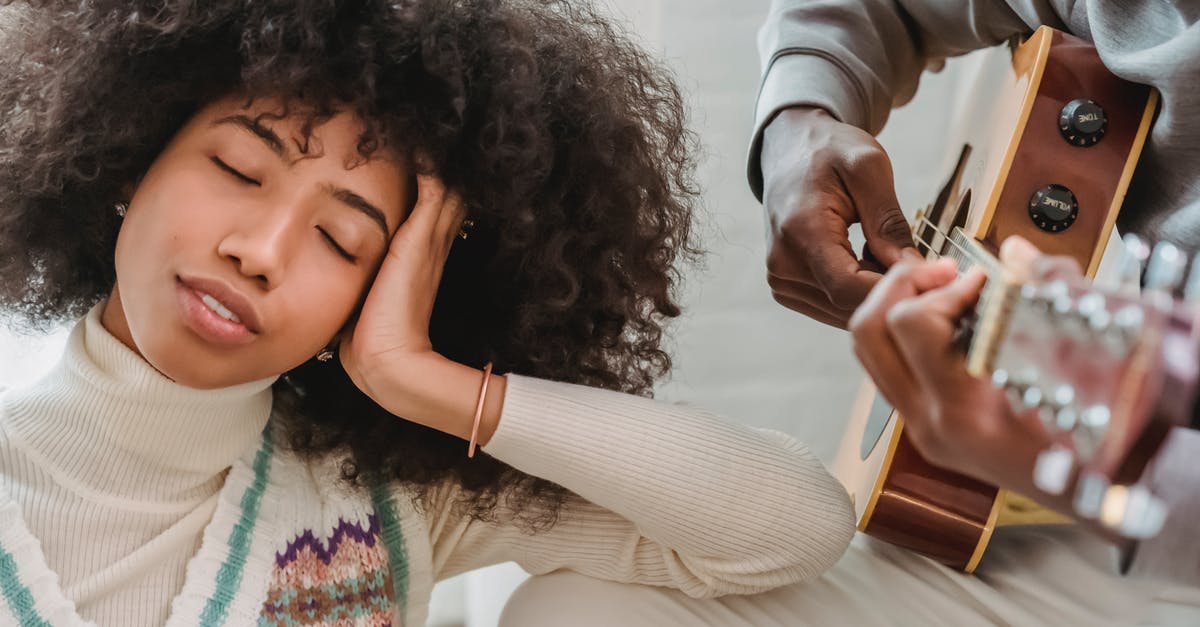 Love Live without the music - Satisfied African American female with closed eyes listening to anonymous black boyfriend playing song on acoustic guitar while spending time together