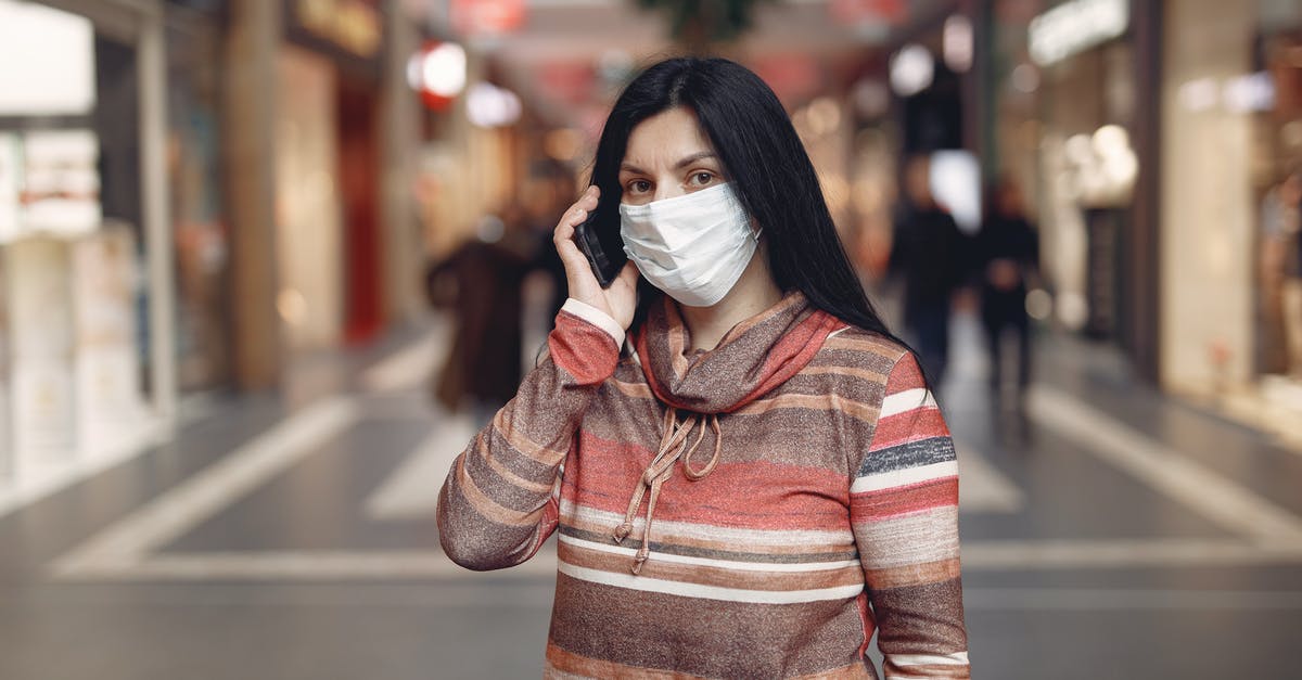 Mêlée cipher character build - Worried casual female wearing protective mask and looking at camera while answering phone call against blurred background in city center during coronavirus pandemic