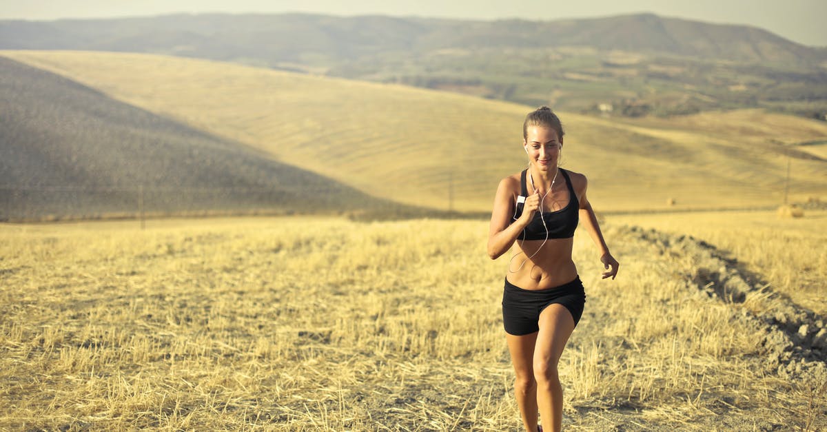 Machines keep using power - Powerful young female athlete in activewear running along hill on background of mountainous landscape and listening to music in earphones during cardio training