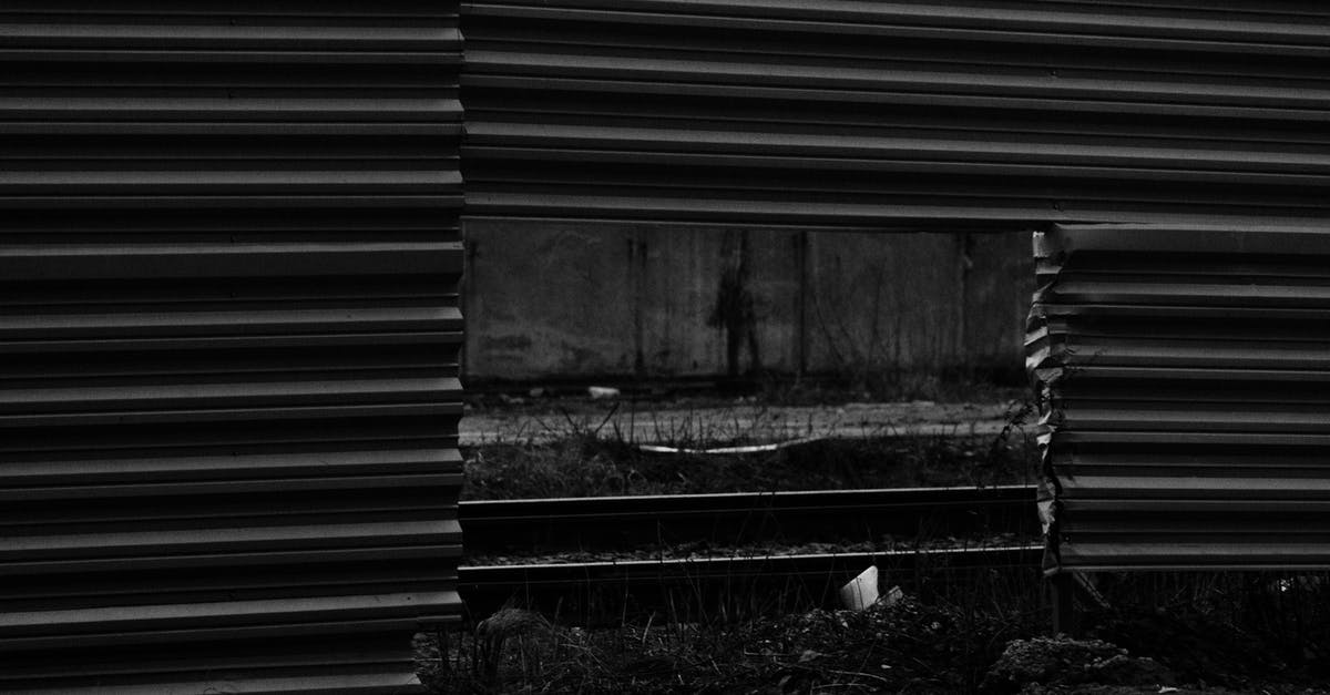 Make barrier blocks visible - Black and white of automobile road and rails visible through square hole in lower part of enclosure from metallic profile