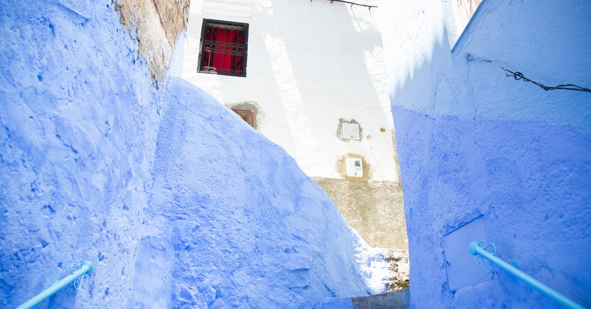 Make barrier blocks visible - Colorful steps with railings between painted blue walls leading to aged stone residential building on sunny street in old town