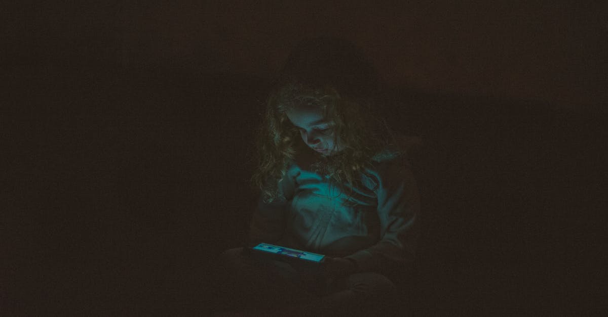 Mid to Late Game Doldrums - Focused  little girl with long curly hair in casual clothes sitting and using smartphone while watching video in dark room