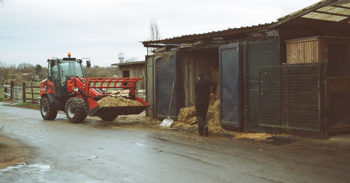 Miners ignore storage barn near the mine - Tractor parked on rural road near anonymous farmer working near barn with hay