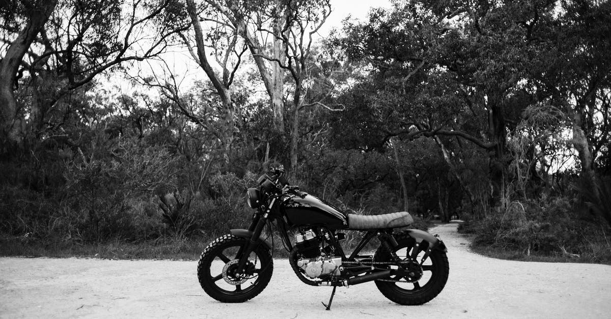 Motor skill: Let speed come naturally? - Black and white of metal motorcycle parked on sandy road near forest with deciduous trees and lush bushes