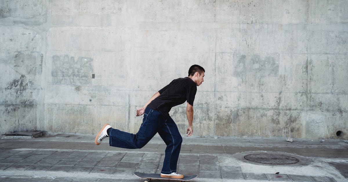 Passing down an ability in Pokémon Black 2 - Full body side view of sportive male in black outfit riding on skateboard near stone wall on pavement in city