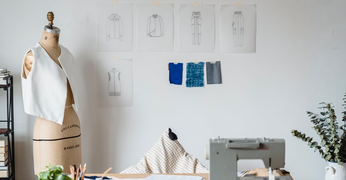 Penalty of removing facility - Table with sewing machine placed near mannequin with garment at white wall with drafts of cloth and samples of textile