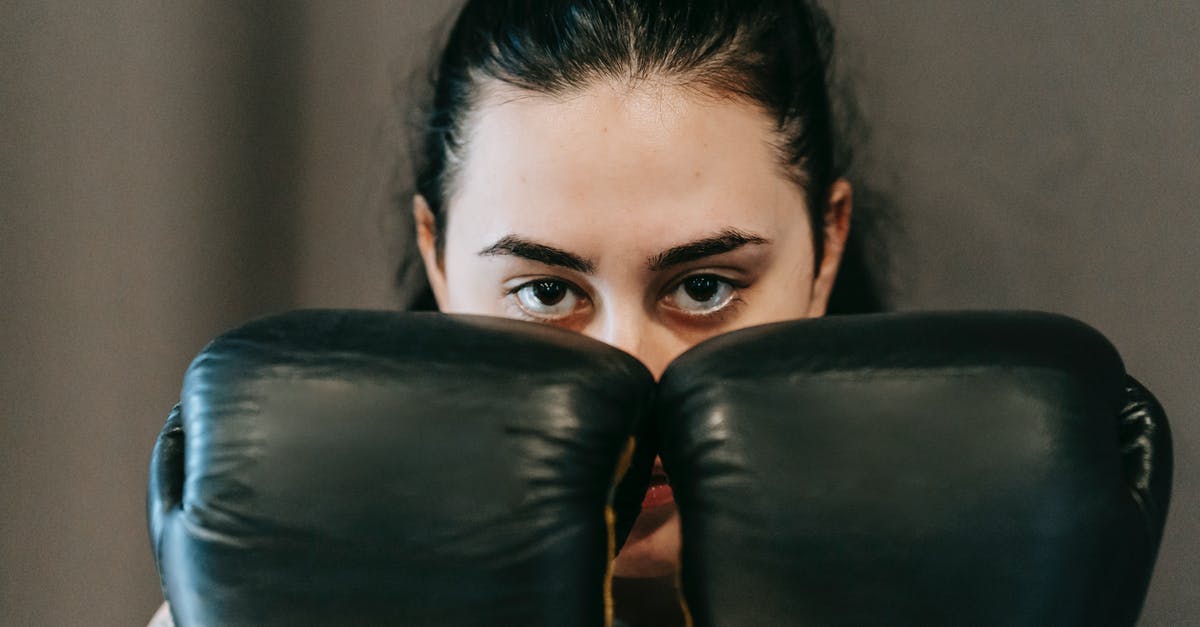 Physical resistance vs. Armor vs. Defence - Concentrated young female athlete with long dark hair covering face with hands in boxing gloves during training