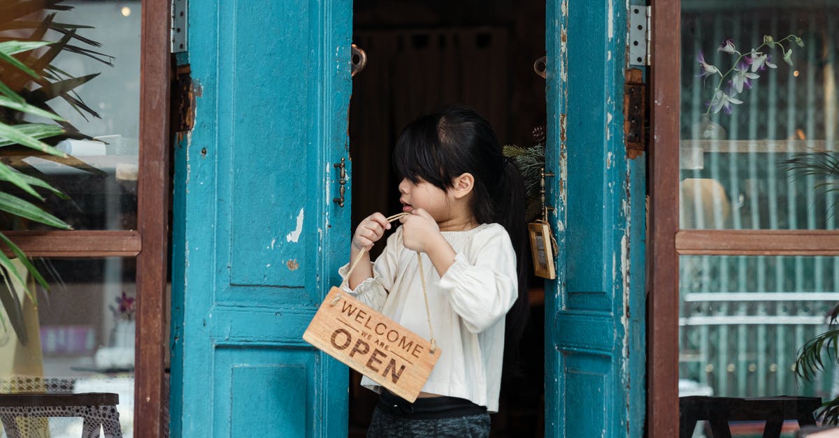 Placing a sign, given from a generator, not working - Photo of Girl Holding Wooden Welcome Signage While Standing on Doorway