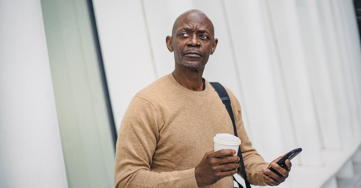 Premature vs Mature town hall - Mature bald black man with smartphone and coffee cup standing on street looking around in downtown