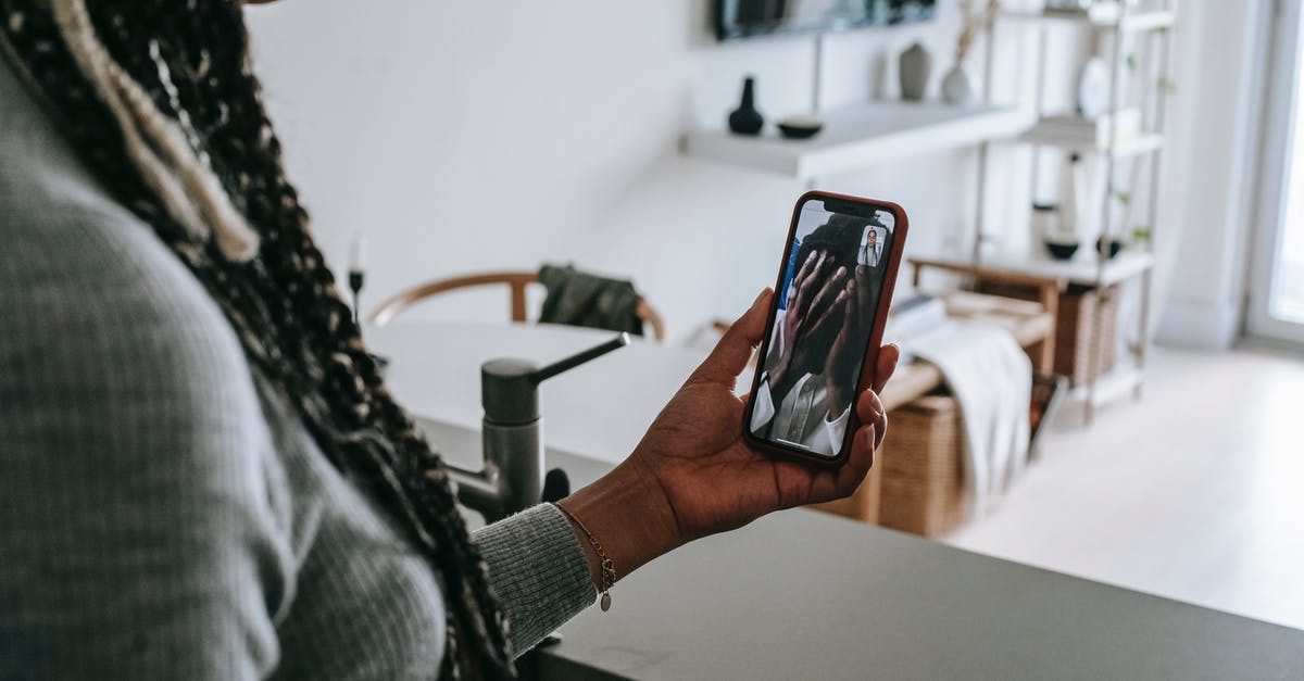 Problem with borderless screen on League of Legends - Crop unrecognizable African American lady with long braids having video call on mobile phone with upset boyfriend covering face with hands while standing in modern kitchen