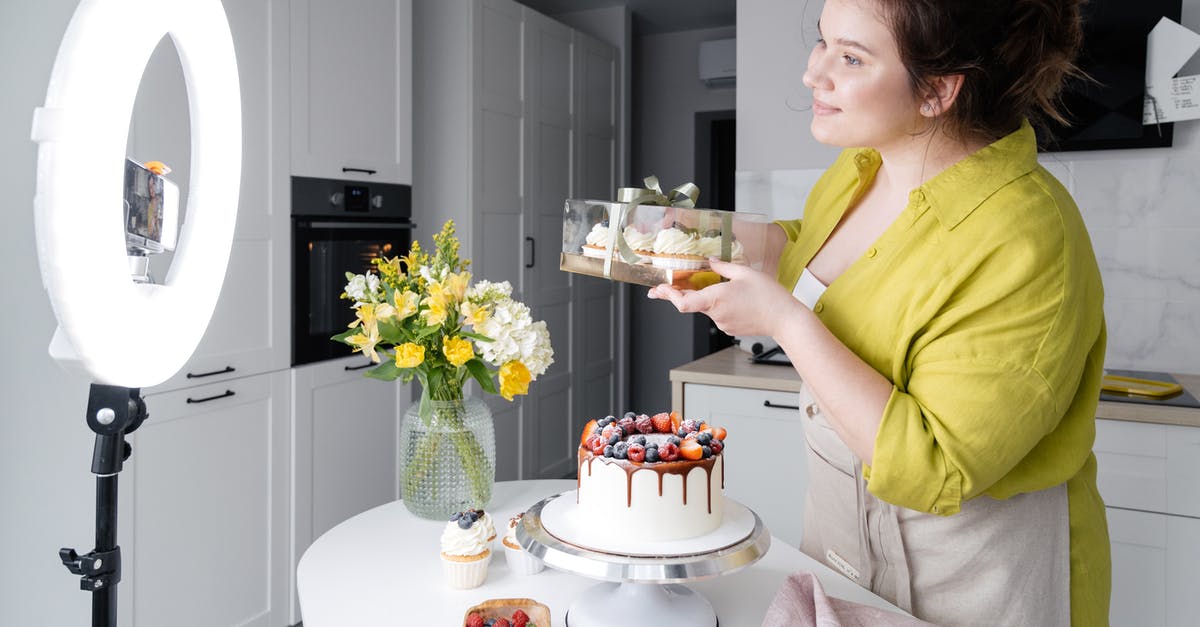 PS4 - Twitch - How do I show comments on-screen while streaming? - Side view of positive young female food blogger in casual clothes and apron introducing yummy cakes and smiling while standing in front of ring lamp and recording vlog on smartphone