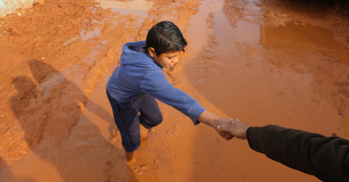 Quest markers stuck on settlement workbenches - High angle of crop person holding hands with ethnic boy stuck in dirty puddle in poor village