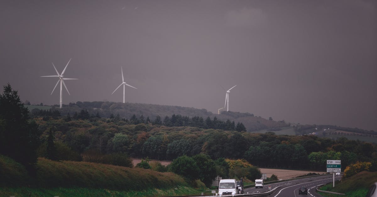 Quickest way to power rank? - Asphalt highway running through grassy lush valley with modern wind turbine generators under gloomy overcast sky