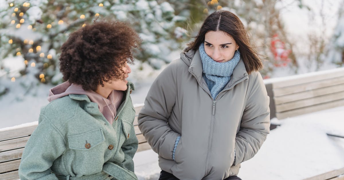 Removing freeze time forever - Diverse female friend talking on bench in winter park