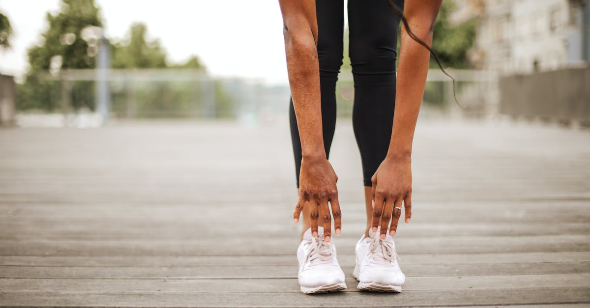 Removing Mercenaries from Hearthstone Training Grounds - From below crop slender female athlete in sportswear and white sneakers doing standing forward bend exercise for stretching body on wooden floor of street sports ground against blurred urban environment in daytime