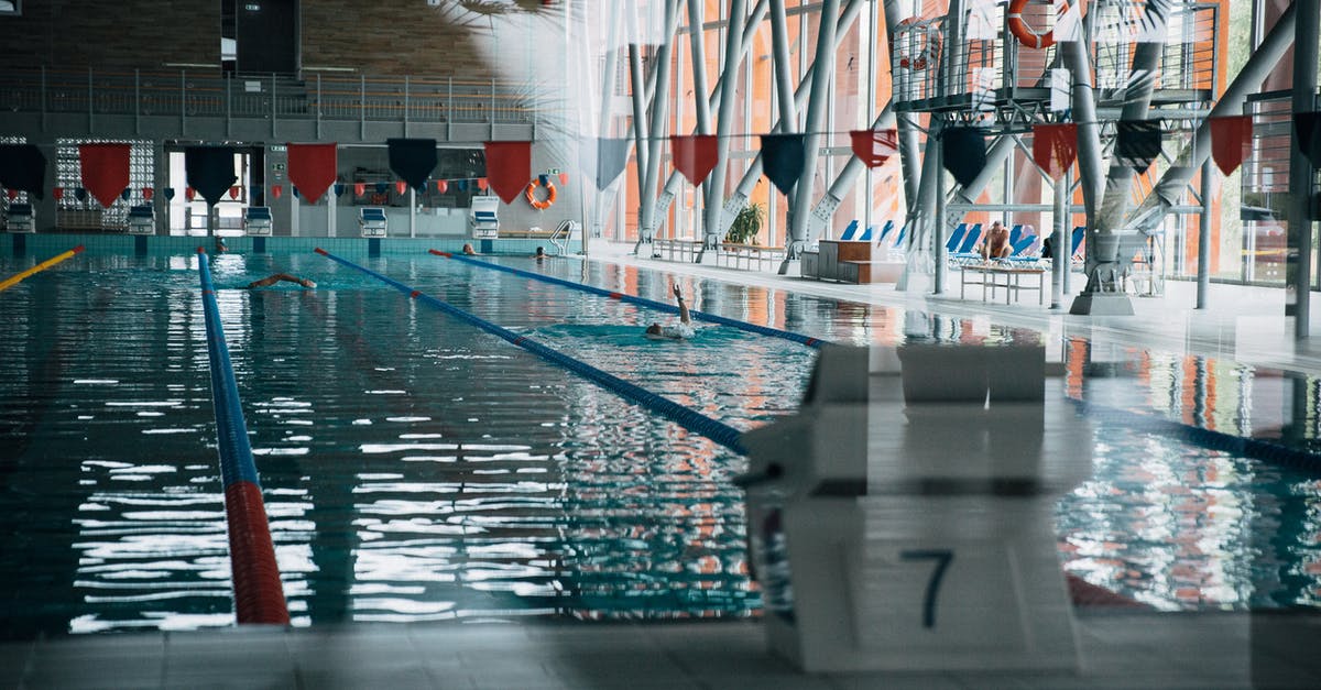 Shiny Jerbolta started to disobey - Through glass wall view of starting platform with number against textile garland above shiny pool with unrecognizable sportspeople swimming during training