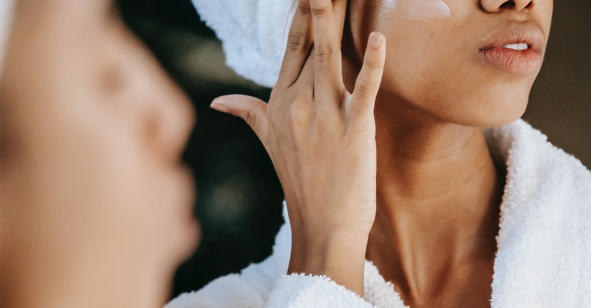 Skin overlay doesn't appear on servers - Crop unrecognizable young ethnic female in terry robe applying moisturizing cream on cheek while reflecting in mirror