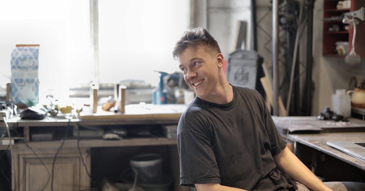 Specialist died before developing weapon - Side view of happy male in working clothes smiling and sitting at table in workshop