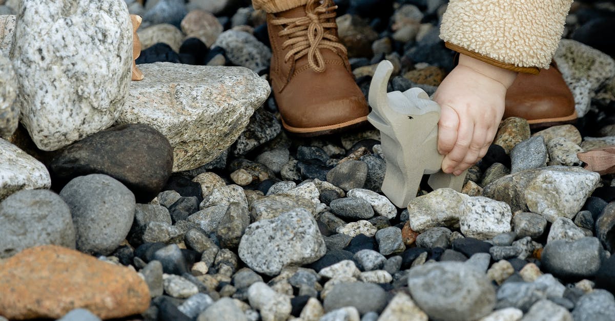 Succeed in baby rocking game in Tomodachi? - Unrecognizable little child in warm clothes and brown boots playing with stone toy of elephant between stones on seashore in winter