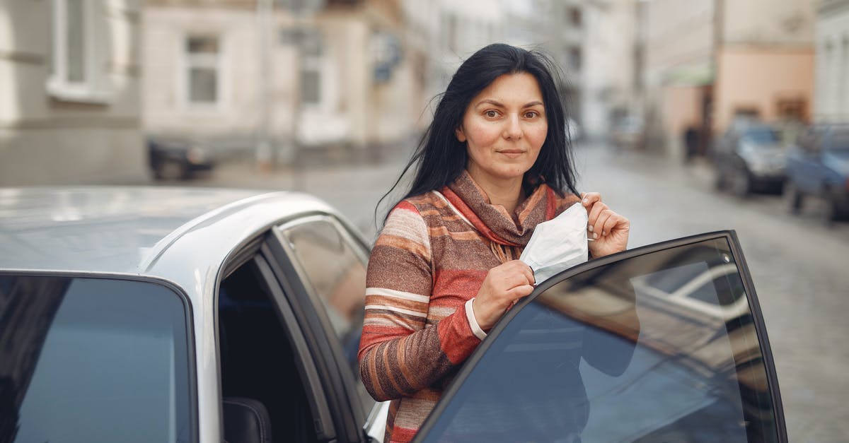 Summon out of the world - Content young woman with medical mask in hands standing near car on urban street