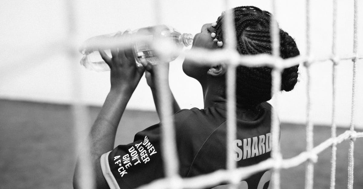 Test if a player has drank a water bottle? - Black and white back view of young female goalkeeper drinking water from plastic bottle