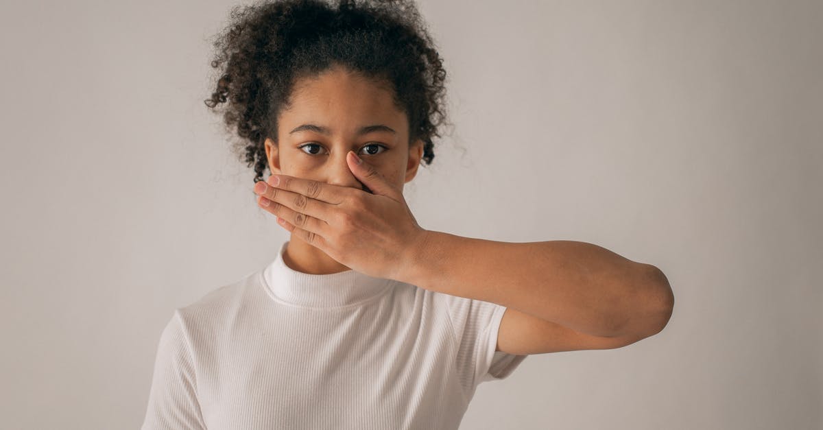 The Moon locked me in secret room during Challange #3 - Concerned African American teenage girl in white outfit looking at camera while covering mouth with hand on gray background in studio