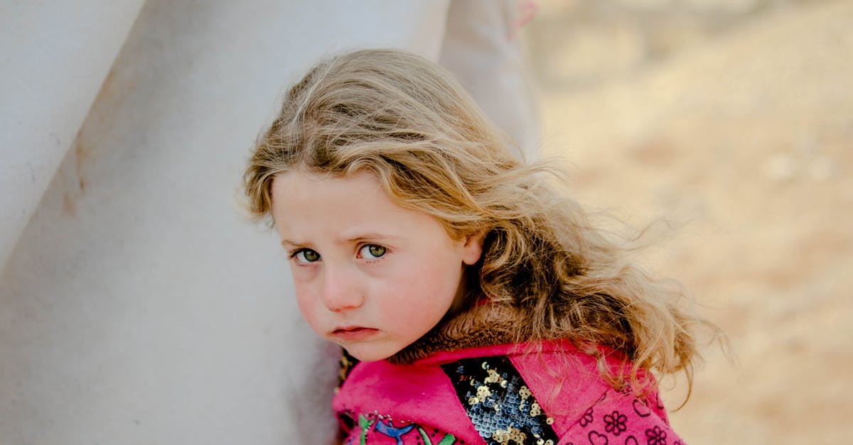 /tp in an area problem - Unhappy little girl looking at camera while standing near weathered shelter in poor refugee camp on blurred background of countryside