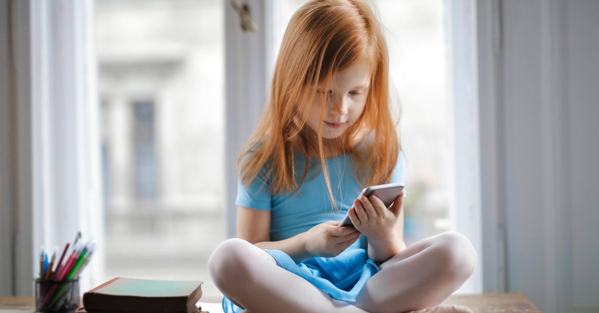 Unable to play RoadRash on Window 10 - Red haired charming schoolgirl in blue dress browsing smartphone while sitting on rustic wooden table with legs crossed beside books against big window at home