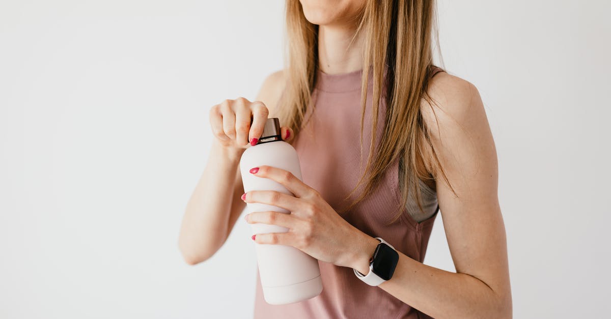 Vessels escaping host bodies over time - Crop faceless young female in casual outfit wearing smart watch opening cosmetic bottle while standing against white background