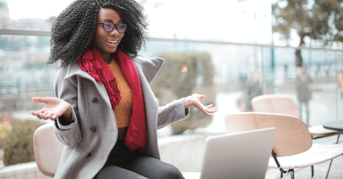 Video Options Not Saving - Happy excited African American female laughing and gesticulating while having video calling on laptop and sitting at modern cafe