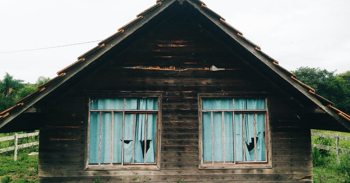 What's the benefit of destroying abandoned dwellings? - Exterior of aged abandoned residential house with shabby windows and torn curtains located on overgrown ground in countryside