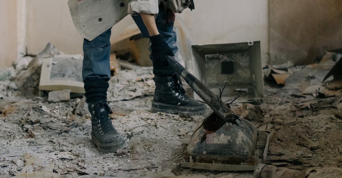 What's the benefit of destroying abandoned dwellings? - Person in Blue Denim Jeans and Black Leather Boots Standing Beside Black Metal Machine