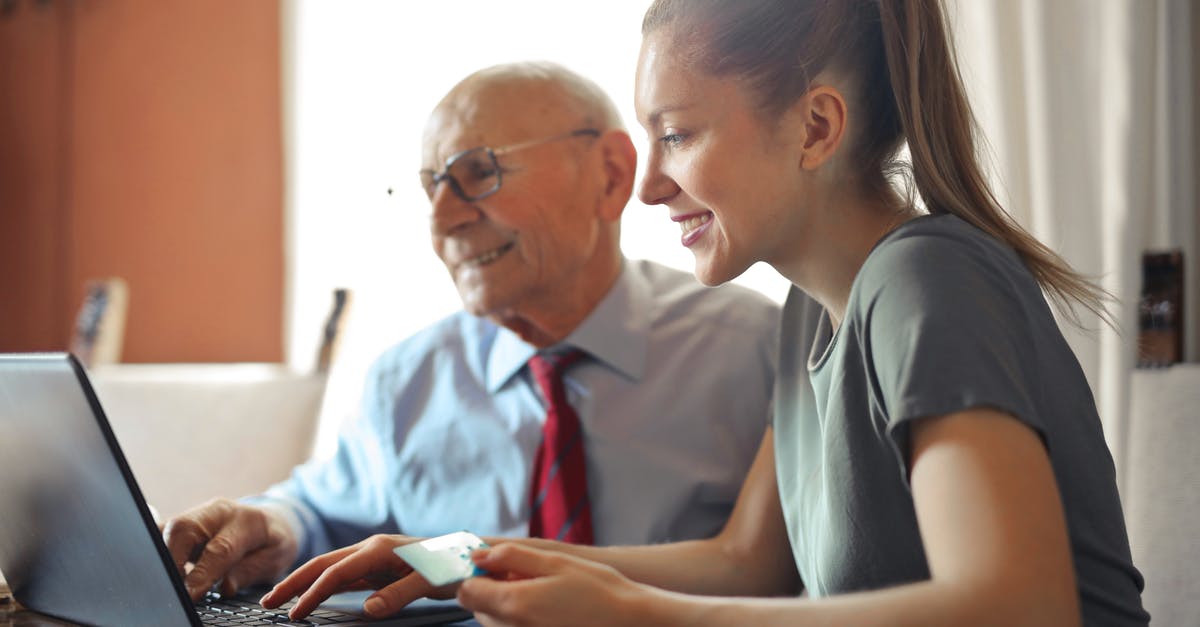 What are Hegemony Credits used for? - Young woman in casual clothes helping senior man in formal shirt with paying credit card in Internet using laptop while sitting at table