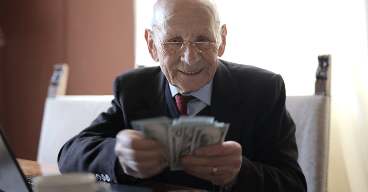 What are the additional privileges earned by an elder? - Positive senior businessman in formal suit and eyeglasses counting money bills while sitting at wooden table with cup of beverage and near opened laptop