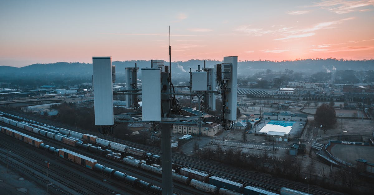 What are the benefits of having a cargo freight station? - Drone view of contemporary cell tower located near railway tracks with cargo containers and wagons against sunset sky