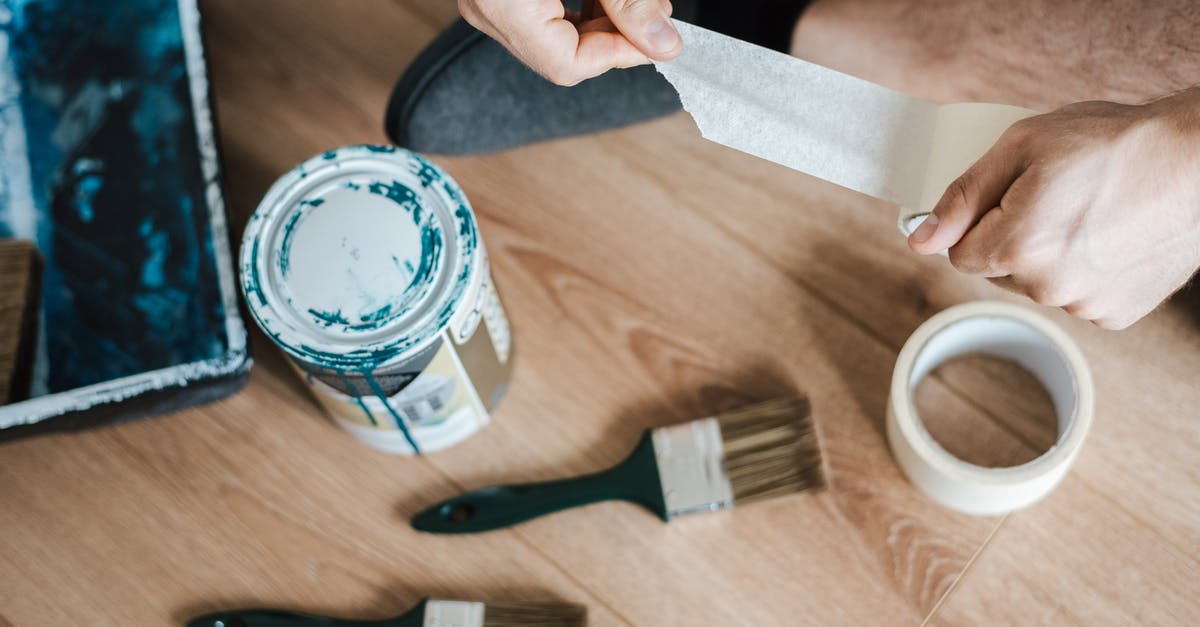 What are the phrases that I can paint? - From above of crop anonymous male unwrapping sticky tape roll on parquet near paint brushes in house