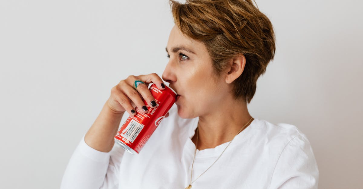 What can I do with the Super-Secret Canadian Mind-Control Device? - Pensive female in white wear with gold necklace and ring on finger drinking cold coke from red can and looking away