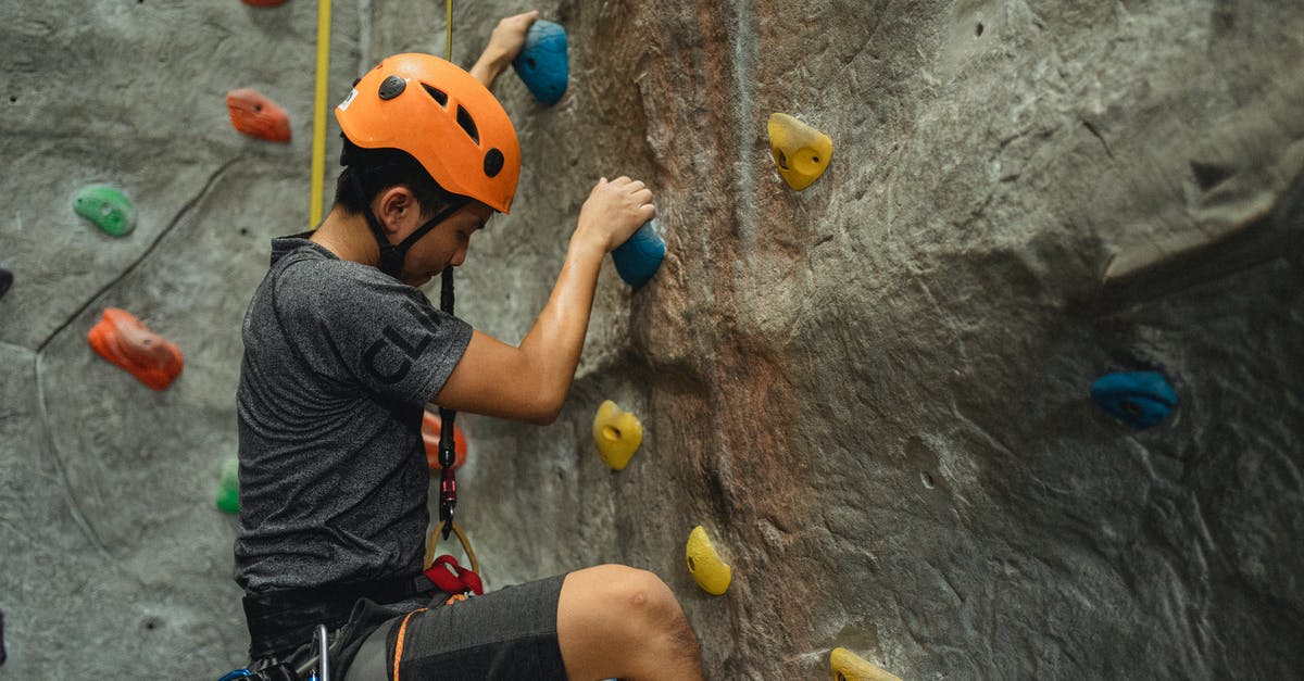 What determines DZ gear score bracket? - Side view of crop young Asian man in orange helmet and belay ascending on climbing wall during training in bouldering center