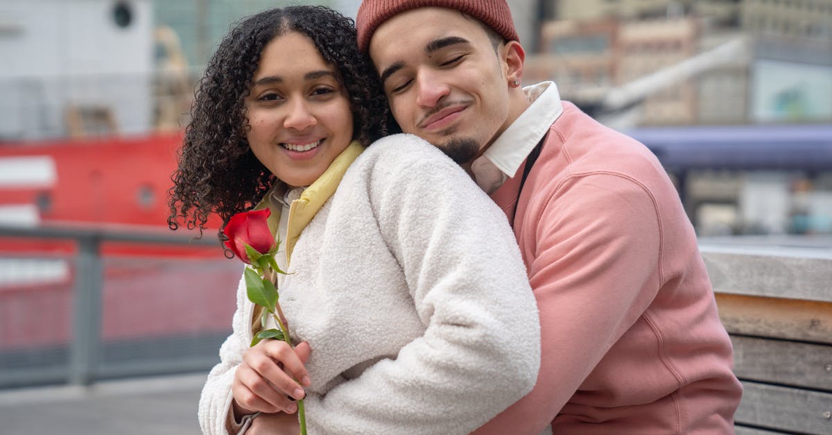 What does a rose coloured ship on the minimap mean? - Smiling Latin American couple in warm clothes with red rose cuddling on wooden bench in city street near buildings and ship in daytime