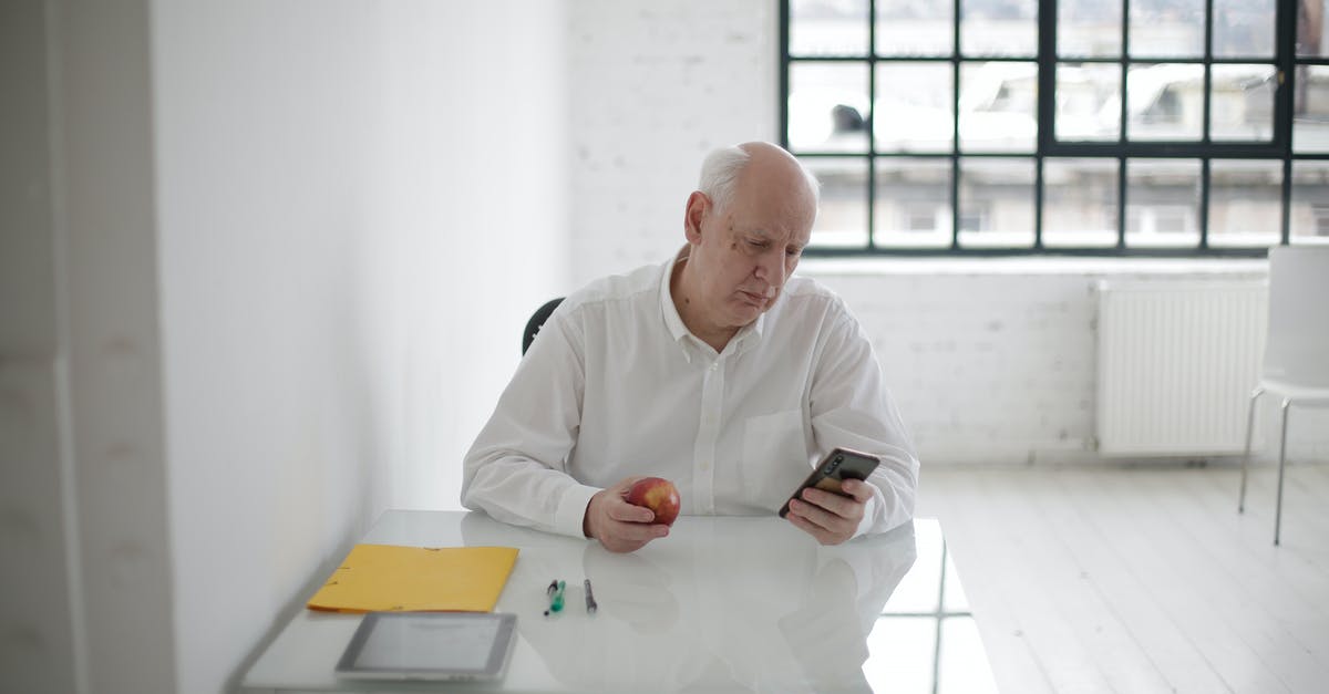 What does the Neko Atsume Apple Watch app do? - Elderly man in white shirt holding apple and messaging on mobile phone during short break in contemporary office