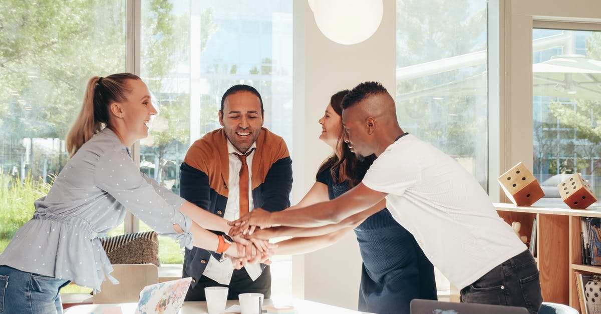 What happens if fewer than three team members are available? - Content multiethnic colleagues joining hands above table with laptops in modern office on sunny day