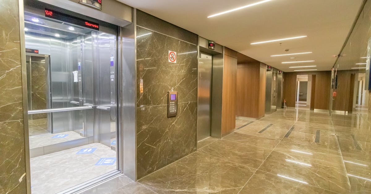 What happens if the level exit is crushed by spikes? - Interior of empty hallway with marble till in wall and floor with opened metal doors of elevator in multistory building